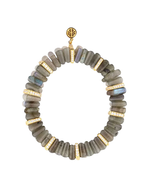 Bracelet made of cylindrical labradorite beads in grayish-green tones with iridescent flashes, accented by gold spacers encrusted with small white gemstones. A round gold charm with an intricate design is positioned at the top.