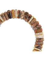 Semi-circular bracelet made of polished cylindrical stones in shades of brown, beige, and gray, accented with gold-colored spacers encrusted with small, clear gemstones.