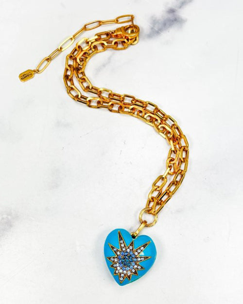 Gold chain necklace with a blue heart pendant on a white marble background