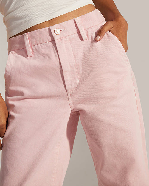 A close-up waist-level view of a model with her hand in her pocket wearing a white crop top and light pink jeans with a white button. The background is grey