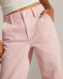 A close-up waist-level view of a model with her hand in her pocket wearing a white crop top and light pink jeans with a white button. The background is grey