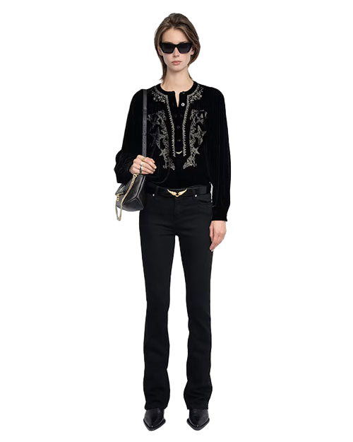 Person wearing black sunglasses, a black long-sleeved top with intricate front embroidery, paired with black pants and holding a small black handbag with gold accents. 