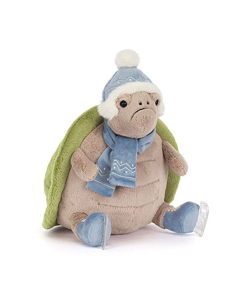 Plush turtle toy with a green shell, wearing a blue winter hat with a white pom-pom, a matching blue scarf with white patterns, and blue ice skates.