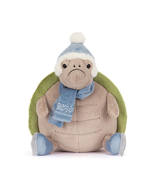 Plush turtle toy with a green shell, wearing a blue winter hat with a white pom-pom, a matching blue scarf with white patterns, and blue ice skates.