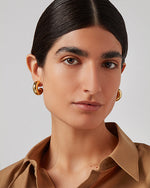 Close-up of gold hoop earrings with, medium-sized and snugly fitting around the earlobes. The person wearing them has a light brown blouse.