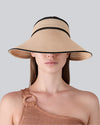 A person wearing a wide-brimmed straw hat with black trim and a one-shoulder knitted top featuring a ring detail on the strap.