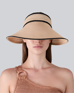 A person wearing a wide-brimmed straw hat with black trim and a one-shoulder knitted top featuring a ring detail on the strap.