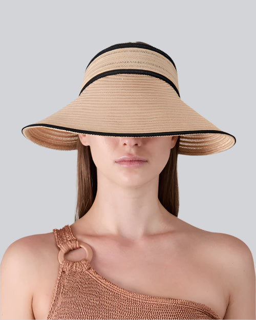 A person wearing a wide-brimmed straw hat with black trim and a one-shoulder knitted top featuring a ring detail on the strap.