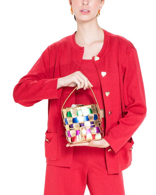 Person in a red outfit with heart-shaped buttons, holding a small colorful woven handbag with a gold handle.