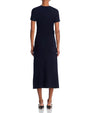 Back view of a person standing upright in a dark, short-sleeved, ankle-length form-fitting dress, wearing pointed-toe low-heel shoes.