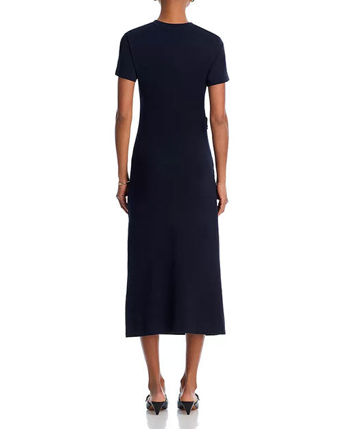 Back view of a person standing upright in a dark, short-sleeved, ankle-length form-fitting dress, wearing pointed-toe low-heel shoes.