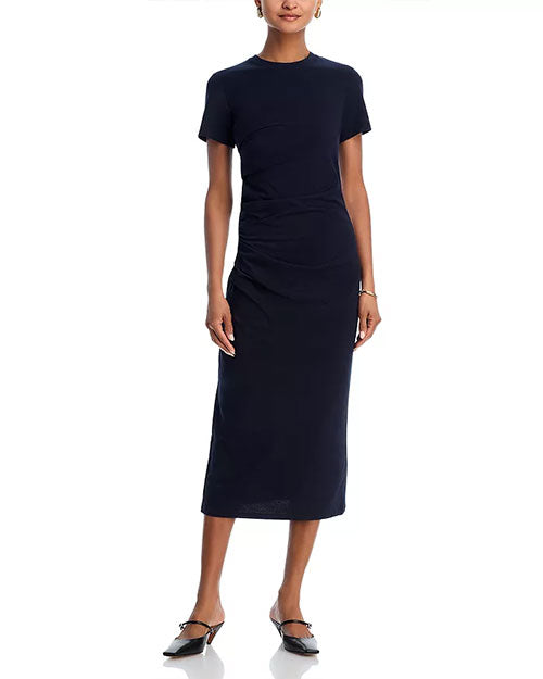Person wearing a fitted, short-sleeved, dark-colored midi dress with side ruching, paired with pointed-toe ankle-strap flats.