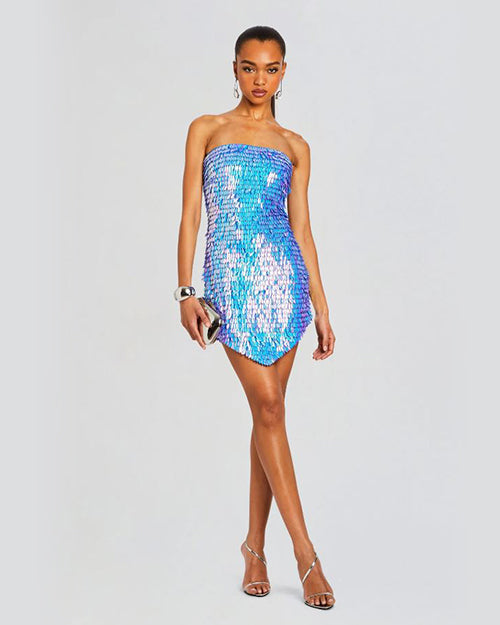 A person wearing a strapless, sequin iridescent blue dress. The hem of the dress is asymmetrical, and the individual wearing silver high-heeled sandals and silver jewelry to complete the look.