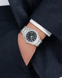 Silver watch on a person's wrist with a dark suit background