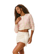 Woman wearing a cropped light pink and white cardigan with bow patterns and white skirt against a plain background