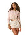 Woman wearing a pink and white patterned cardigan and skirt against a plain background