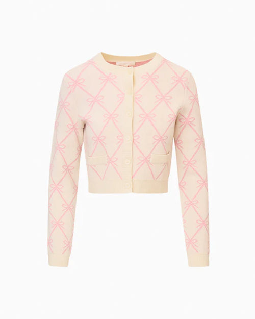Light-colored long-sleeved cardigan with pink bow patterns, round neckline, front buttons, and two small pockets on the lower front, displayed against a plain white background.