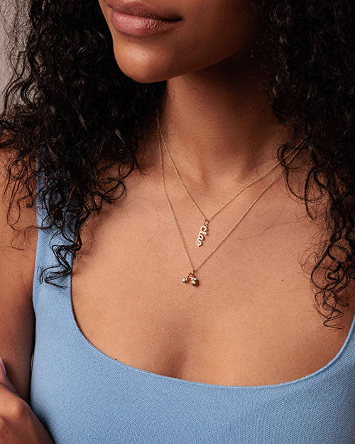 A close up of a person's neck wearing a blue top and two gold neckless.