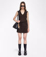 A full body frontal view of a brunette model wearing a matching set including a brown V-neck tank-top with white rhinestone designs shoulders, and a skirt with two pockets in front. She is also wearing black sunglasses, a black purse with multiple charms hanging from it, and black chunky boots. The background is plain white.