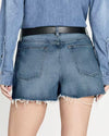 Back view a model in denim shorts with frayed hem. Denim shorts paired with denim shirt, black belt and black heel.