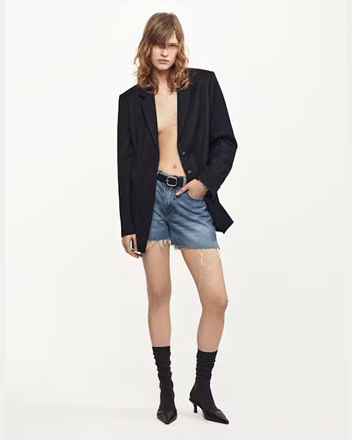 A pair of faded blue denim shorts styled with a black blazer, black belt, and black kitten pointed heels with sheer black socks for a trendy model off duty look. 