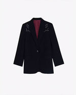 A full view of a black blazer with white embroidery on the shoulders, and a maroon-colored inside. The background is plain white.