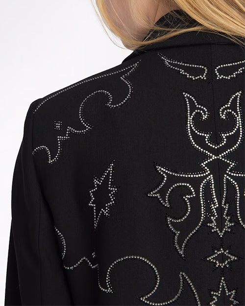 A close-up backside view of a model's shoulder adorned with a black jacket featuring an intricate white embroidery on the back and black pants. 