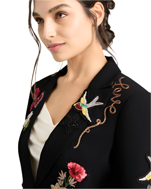 A close up of a person wearing a blazer with colorful embroidery of flowers, birds, and "LOVE"