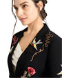 A close up of a person wearing a blazer with colorful embroidery of flowers, birds, and "LOVE"