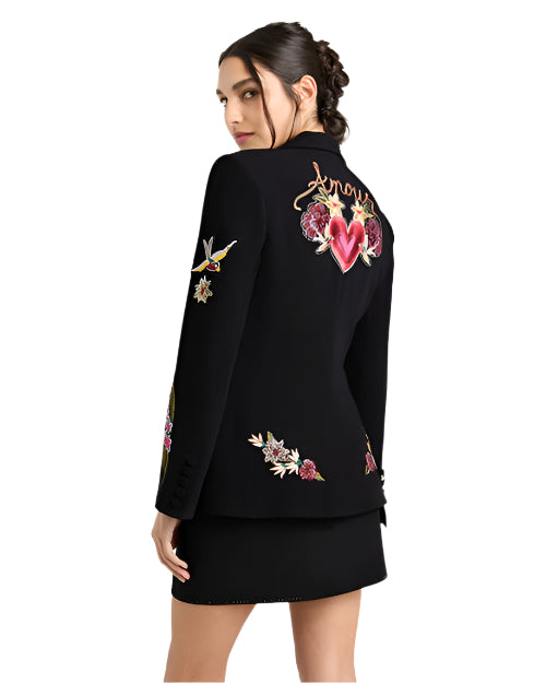 Back view of a person in a black blazer with colorful embroidery, including a heart with 'Amore' and floral designs.