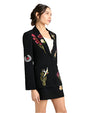 Person in black blazer and skirt with colorful floral and nature-themed embroidery, standing against a light background