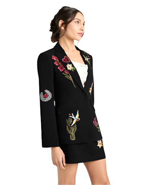 Person in black blazer and skirt with colorful floral and nature-themed embroidery, standing against a light background