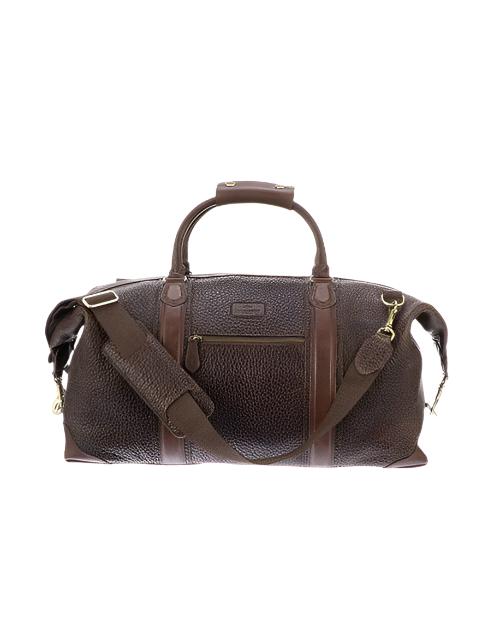 A brown duffle bag with a textured surface, featuring leather handles and a detachable, adjustable shoulder strap. The bag has brass hardware, a front pocket with a logo patch, and top zipper closure.