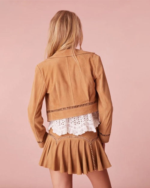 Model showing the back of the brown leather oitfit. Model wearing a stylish brown jacket and matching brown skirt, posed against a pink background.