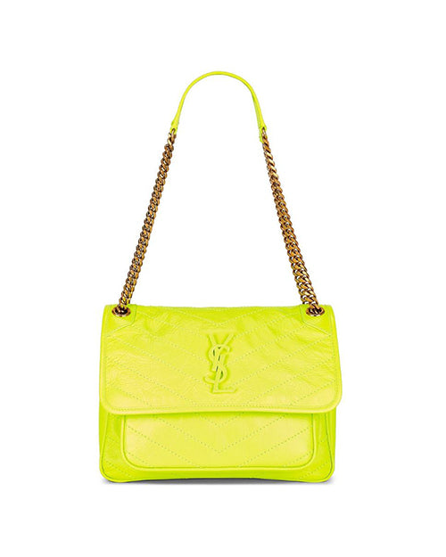 A highlighter yellow leather shoulder bag with a prominent gold-toned metal logo resembling the letters ‘YSL’ intertwined on the flap. The bag features a structured rectangular shape with rounded corners and visible stitching that creates a padded effect. It has a chain-link shoulder strap with leather threaded through it, also in white, which is partially draped over the bag’s surface.