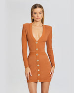 A close-up orange long sleeve dress, with gold buttons. The dress has a low V-neck plunge, and metallic material. The dress has small shoulder padding for a suited affect.