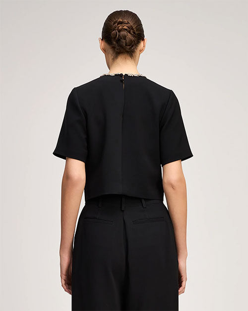 Rear view of a black short-sleeved top paired with high-waisted black pleated trousers.
