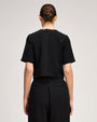 Rear view of a black short-sleeved top paired with high-waisted black pleated trousers.