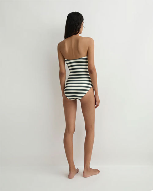 Rear view of a person wearing a strapless, horizontally striped one-piece swimsuit in green and white against a plain light background.