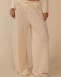 A person wearing loose, wide‑leg pants made from a cream-colored textured fabric with a nubby, boucle‑like surface. The pants have a relaxed fit and feature a drawstring waistband with ties at the front.