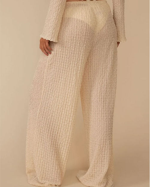 Back view of a person wearing loose, wide‑leg pants made from a cream-colored textured fabric with a nubby, boucle‑like surface. The pants have a relaxed fit and feature a drawstring waistband with ties at the front. 
