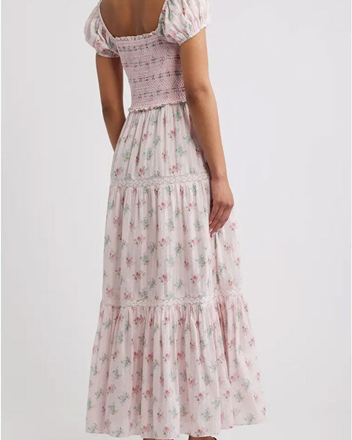 Rear view of a light pink floral maxi dress with short puff sleeves, smocked bodice, wrap-style V-neckline, and tiered ruffle skirt.
