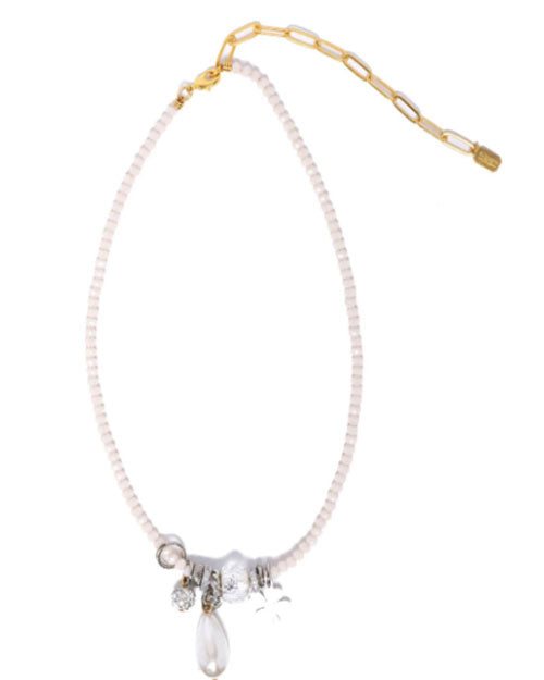 A delicate necklace with small white beads and a gold chain extender, featuring silver charms and a clear teardrop pendant clustered at the center, displayed on a white background.