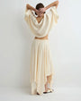Rear view of a person modeling a soft cream long-sleeve cropped top with a round neckline and matching flowing midi skirt, paired with light-colored flat sandals against a plain light background.