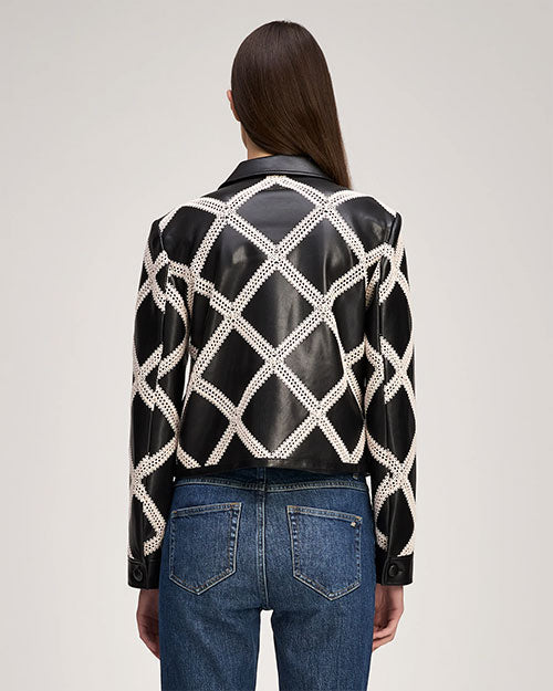 Rear view of a person wearing a cropped black leather jacket with an ivory diamond-pattern overlay and front zip closure, paired with a black top and blue jeans.