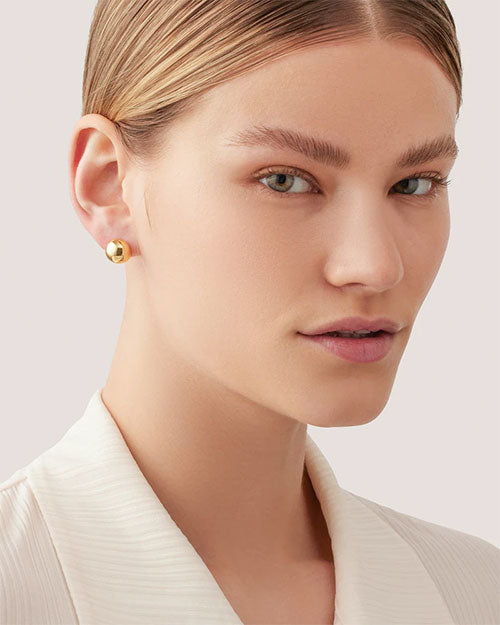 Close-up of a person wearing a small, chunky gold hoop earring with a smooth, polished finish.