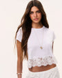 Person with long dark hair wearing a white cropped T-shirt with a scalloped lace hem, a pendant necklace, and matching white lace bottoms against a light background.