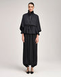 Person wearing a black ruffle-neck peplum top with a tie-front detail, voluminous sleeves, and matching wide-leg pants with gathered hems, paired with pointed black shoes.