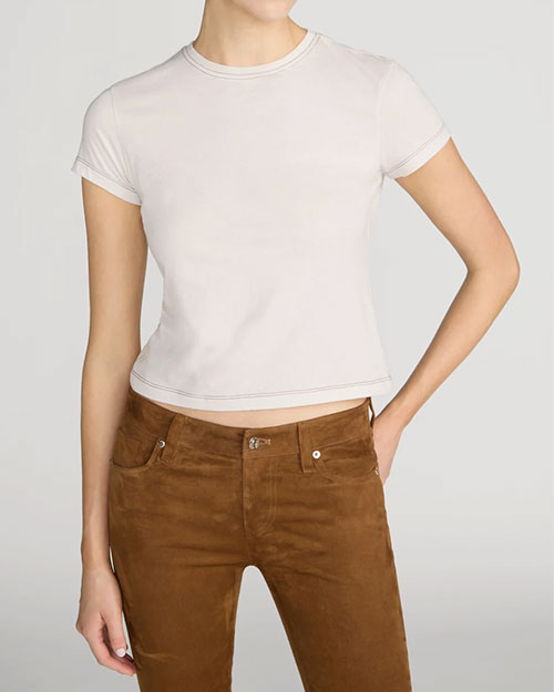 A person wearing a beige baby tee with brown contrast stitching. 