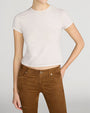 A person wearing a beige baby tee with brown contrast stitching. 